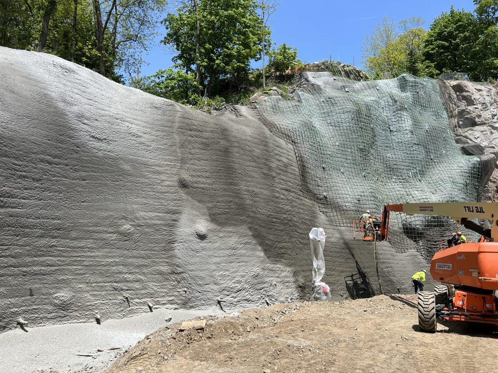 Cliffside stabilized with shotcrete, with one side completed and the other side prepped with blue wire mesh for shotcrete application.