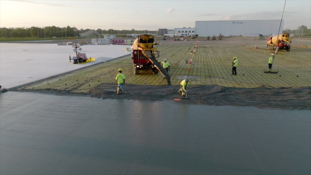 Large industrial concrete flatwork pour with multiple workers raking the concrete.