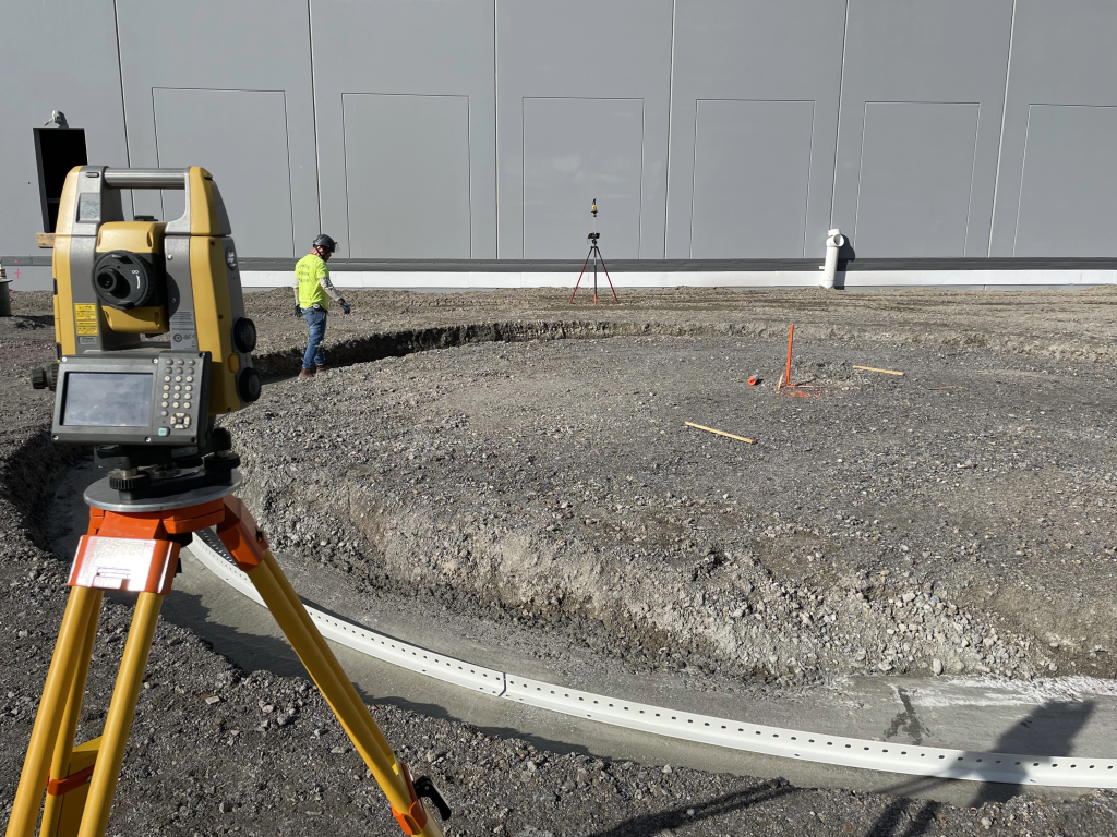 Surveying equipment next to a worker preparing tank ring foundations.