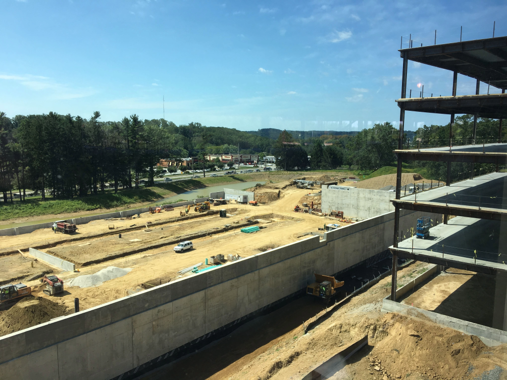 An aerial view of a large construction site with concrete foundation walls, earthwork, equipment, and an emerging building structure.