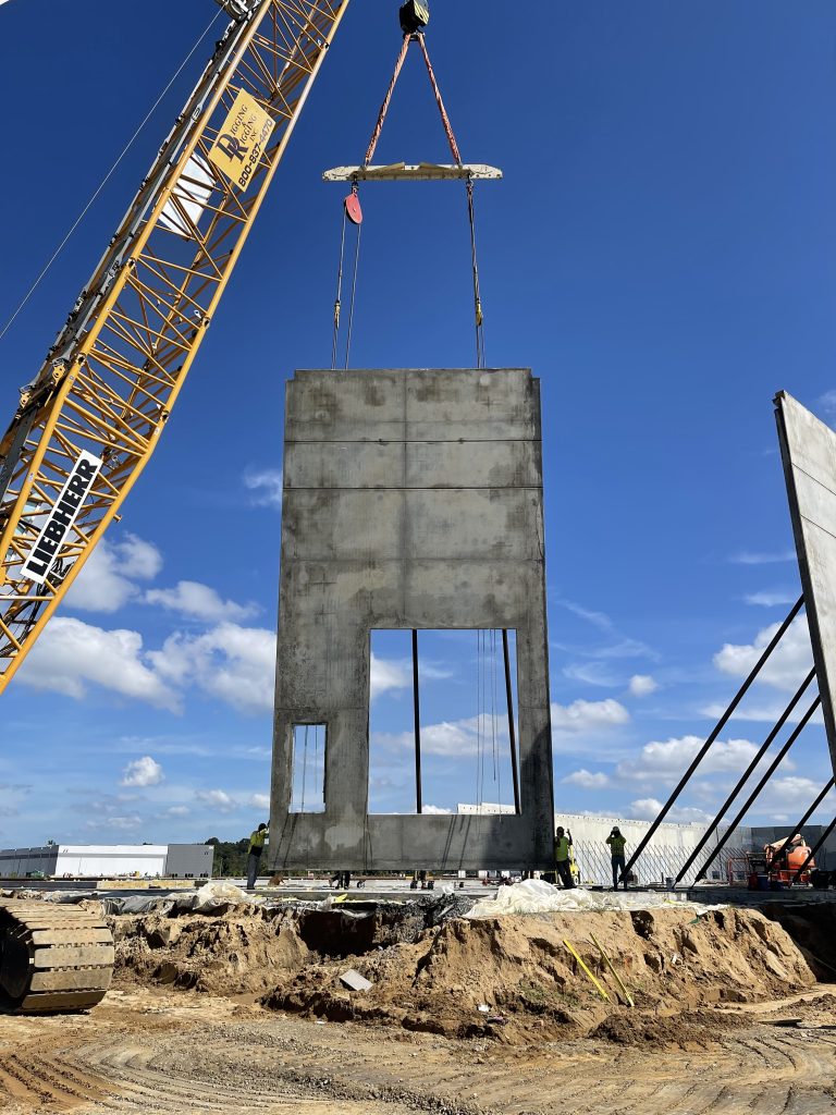 A crane lifting a singular concrete tilt-up wall panel.