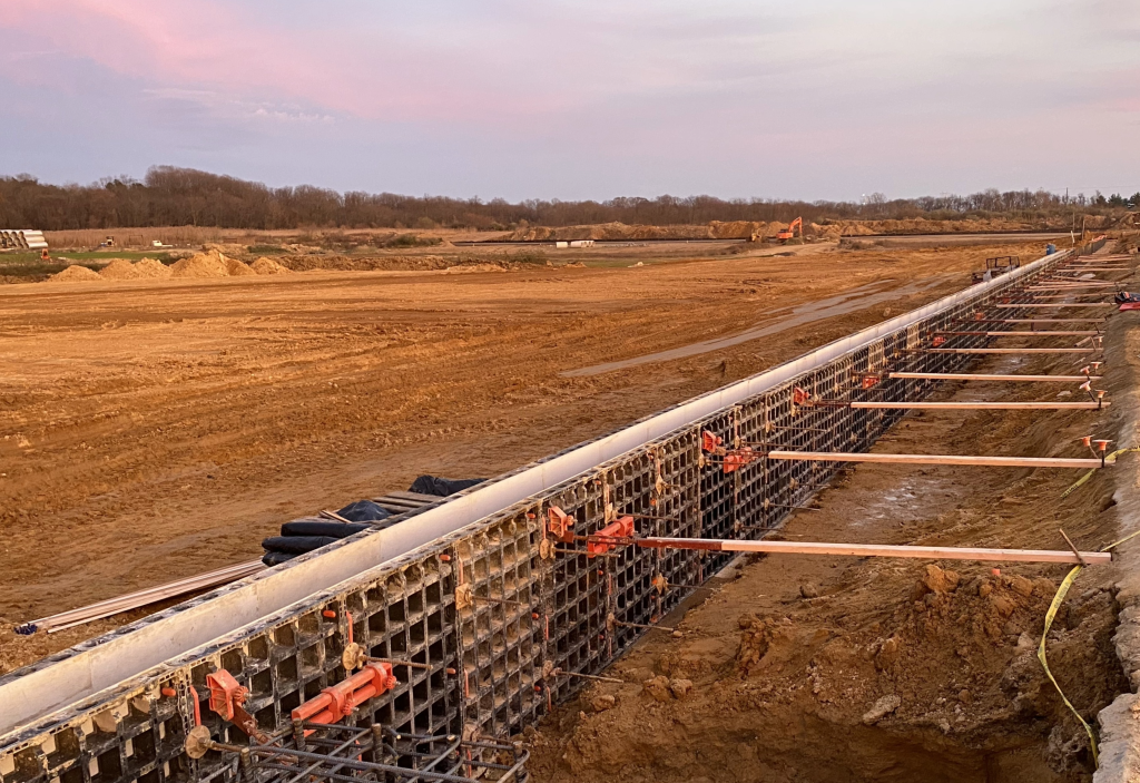 A long concrete foundation wall prepared for a pour on a large site.