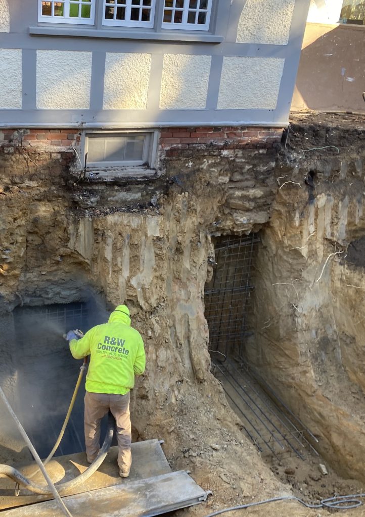 2 underpins underneath a building being prepped and shot with shotcrete by a nozzleman.