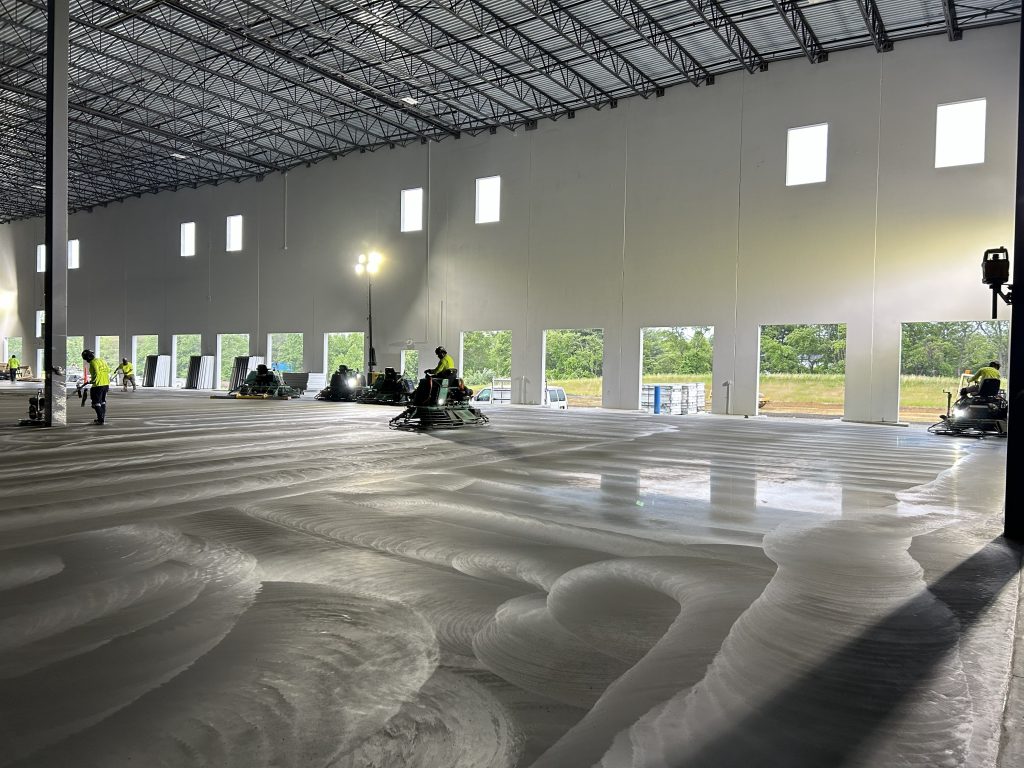 Ride-on trowel finishers on a shiny concrete pour in a covered building.
