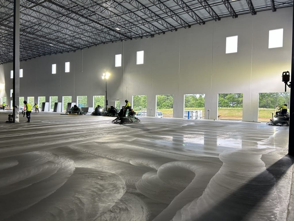 Ride-on trowel finishers on a shiny concrete pour in a covered building.