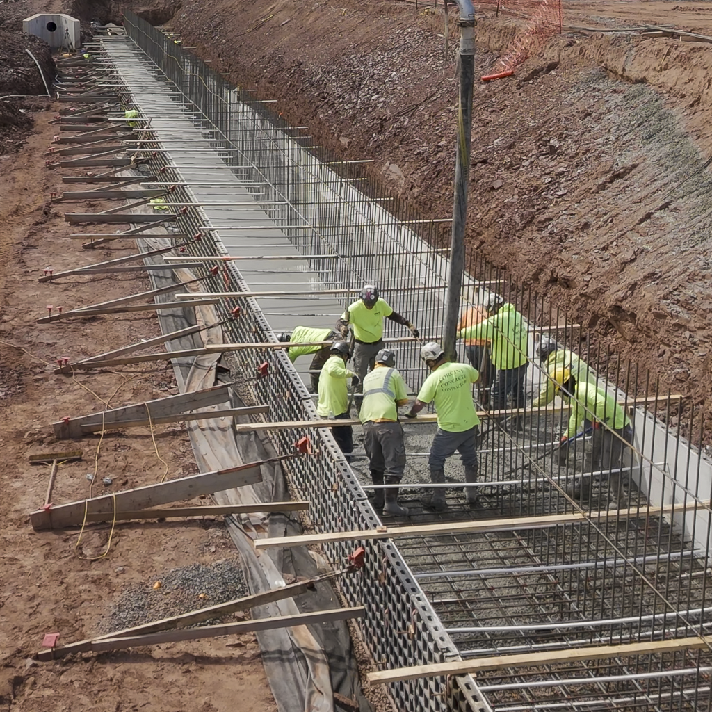 322-foot-long retaining wall footing being poured by concrete construction workers.