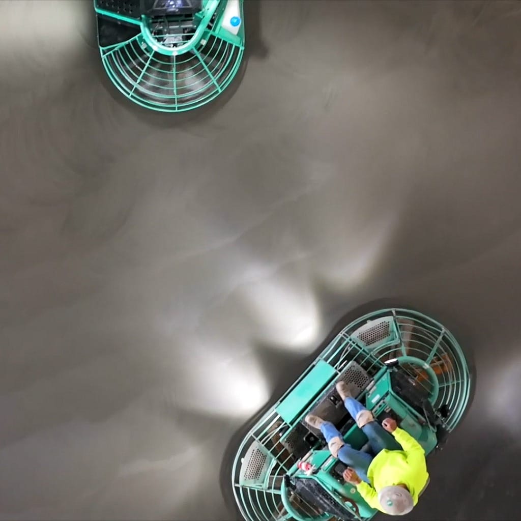 Overhead shot of 2 finishers on ride-on trowels finishing a concrete surface.